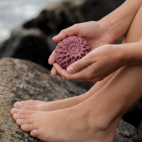 Händer som håller en rosa fast balsamkaka Kamomill Velvet vid havet